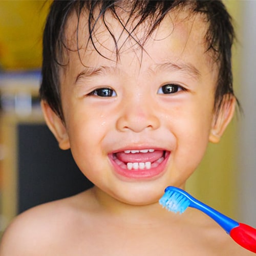 A little boy learning to brush his teeth while laughing